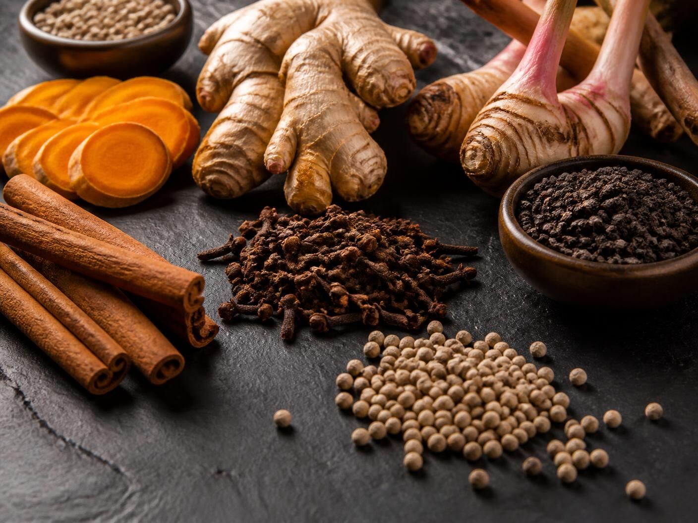 Indonesian cinnamon, cloves, turmeric, ginger, galangal and peppercorns on dark slate